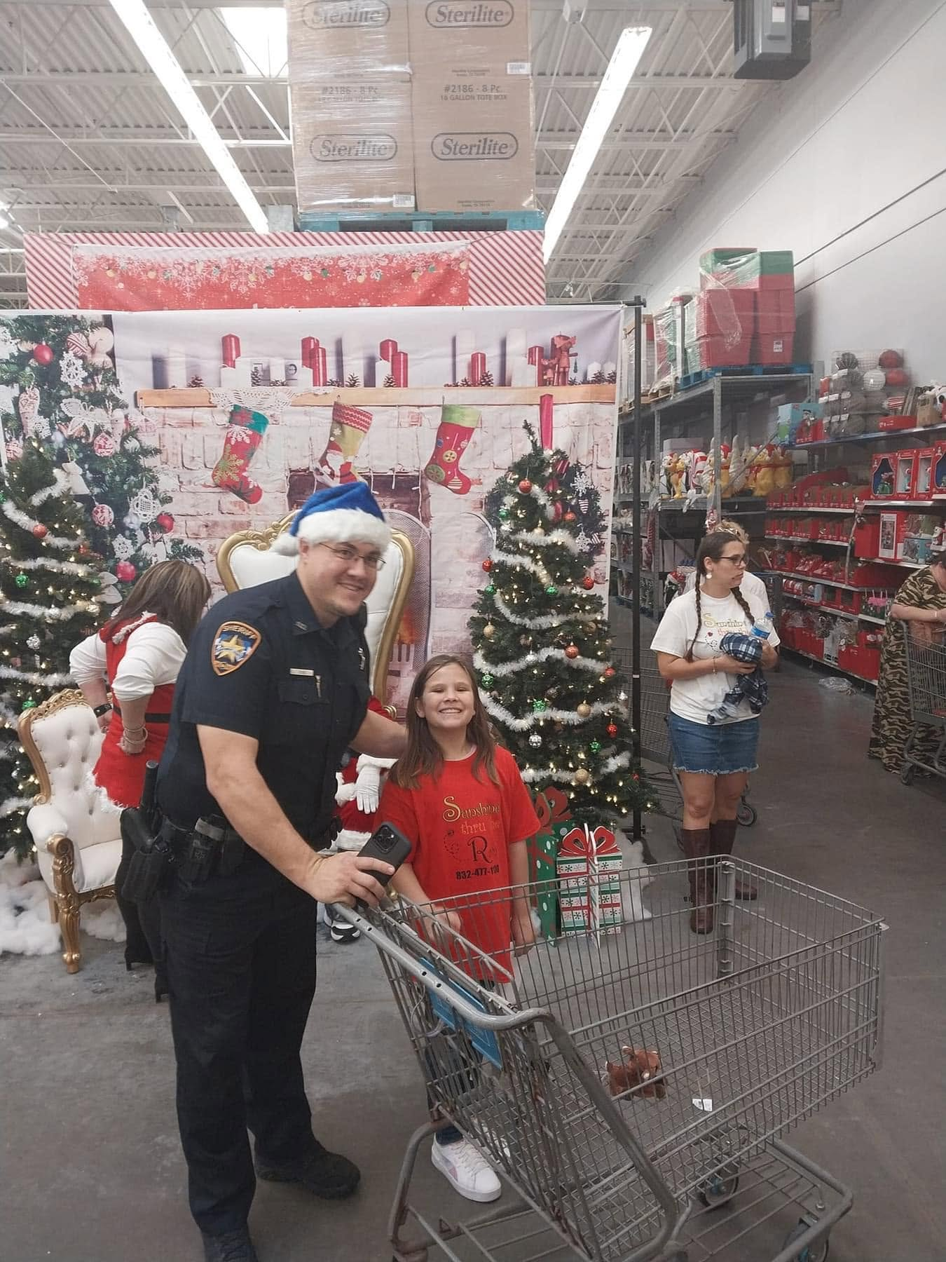 An officer and a child stand beside a shopping cart at a Christmas shopping event