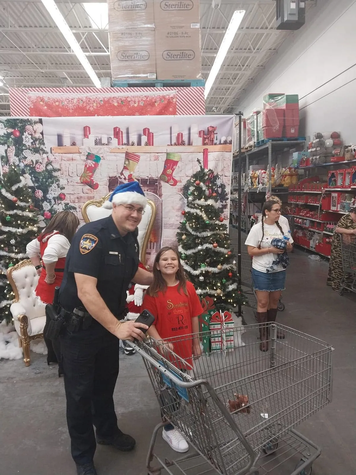 An officer and a child stand beside a shopping cart at a Christmas shopping event